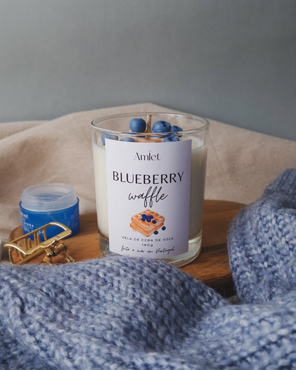 Vela em copo transparente com aroma de baunilha e mirtilos e com o topo da vela decorado com um waffle e vários mirtilos 